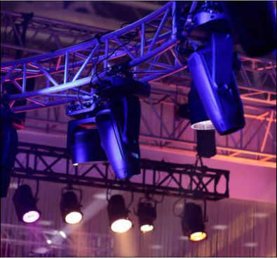 Overhead stage lighting rig featuring spotlights and wash lights with purple ambient theater lighting.