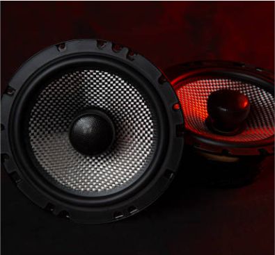 Two high-end audio speakers with carbon fiber cones displayed under dramatic red studio lighting.