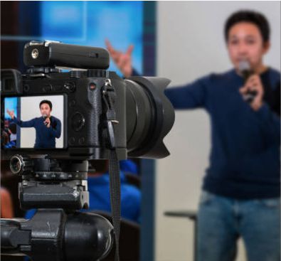 Close-up of a digital camera screen showing a male presenter speaking into a microphone during a live stream session.